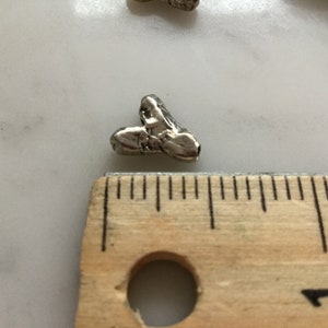 May include: A silver heart-shaped charm with a textured surface. The charm is approximately 1.25 cm in size and is next to a ruler.