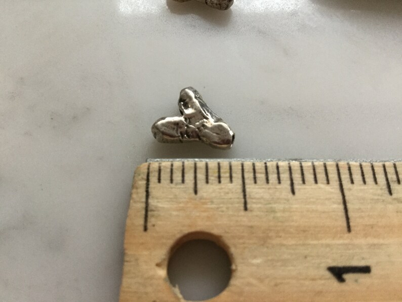 May include: A silver heart-shaped charm with a textured surface. The charm is approximately 1.25 cm in size and is next to a ruler.