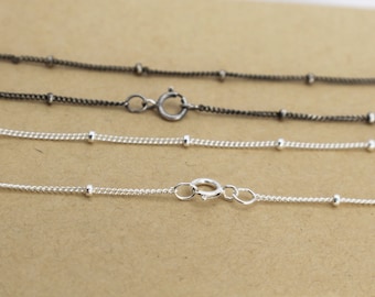 May include: Three silver chains with small beads, two are silver and one is black, all with a clasp.