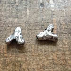 May include: Two silver-coloured heart-shaped beads with a rough, textured surface. The beads have a hole through the top for stringing.