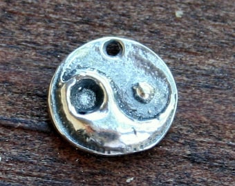 May include: A silver charm in the shape of a yin yang symbol. The charm has a textured surface and a hole at the top for attaching to a chain or bracelet.