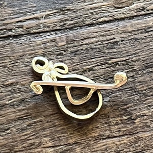 May include: A gold-colored metal brooch in the shape of a stylized letter 'G'.