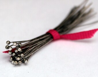 May include: A bundle of silver-toned head pins with round heads, tied together with a bright pink ribbon.