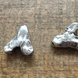May include: Two silver metal charms shaped like a heart. The charms are textured and have a rustic look.