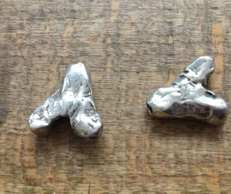 May include: Two silver metal charms shaped like a heart. The charms are textured and have a rustic look.
