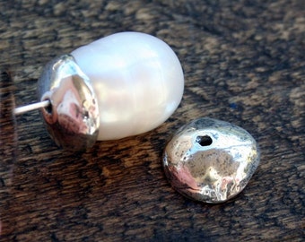 Può includere: Un orecchino di perla bianca con una montatura in argento. L'orecchino è composto da una singola perla grande che è fissata a un perno d'argento. Il perno è fissato a un retro in argento a forma di piccolo disco piatto.