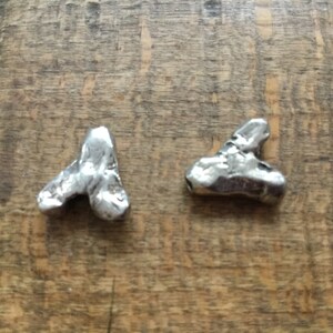 May include: Two silver metal charms shaped like triangles. The charms are textured and have a rough, organic look.