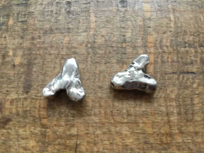May include: Two silver metal charms shaped like triangles. The charms are textured and have a rough, organic look.
