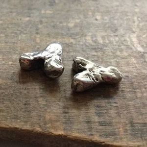 May include: Two silver, heart-shaped charms with a rough, textured surface. The charms are made of metal and have a rustic, handmade look.