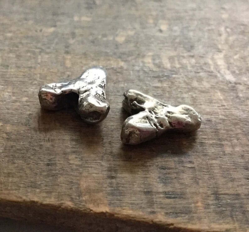 May include: Two silver, heart-shaped charms with a rough, textured surface. The charms are made of metal and have a rustic, handmade look.