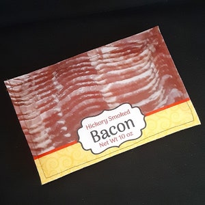 May include: A close-up of a package of hickory smoked bacon. The package is yellow and red with the words "Hickory Smoked Bacon Net Wt 10 oz" printed on it.