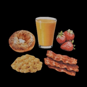 May include: A breakfast spread on a black background. It includes a bagel with cream cheese, a glass of orange juice, a pile of strawberries, a serving of scrambled eggs, and strips of bacon.