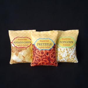 May include: Three yellow fabric snack bags with different snack options. The bags are labeled "Snack Size Potato Chips Lightly Salted", "Snack Size Pretzels Lightly Salted", and "Snack Size Popcorn Buttered".