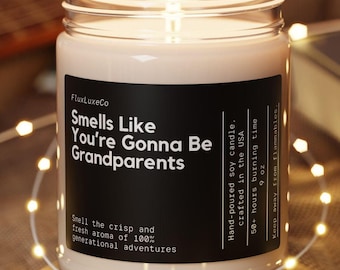 May include: A lit soy candle in a glass jar with a black label that reads "Smells Like You're Gonna Be Grandparents." The candle sits on a wooden coaster, surrounded by string lights. The background includes a guitar and a book.