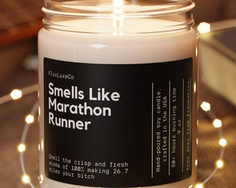 May include: A lit soy candle in a glass jar with a black label that reads "Smells Like Marathon Runner." The candle sits on a wooden coaster, surrounded by string lights. The candle is hand-poured in the USA and has a 50+ hour burn time.
