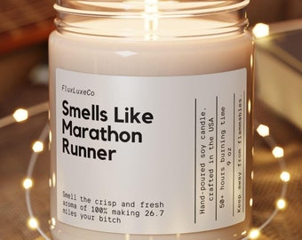 May include: A lit soy candle in a glass jar with the text "Smells Like Marathon Runner." The candle sits on a wooden coaster, surrounded by string lights. The label also states it is hand-poured, crafted in the USA, and has a 50+ hour burn time.