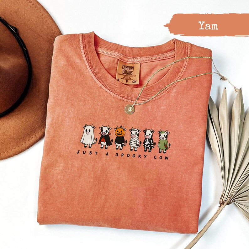 Orange t-shirt with cartoon cows dressed in Halloween costumes and text "Just A Spooky Cow".