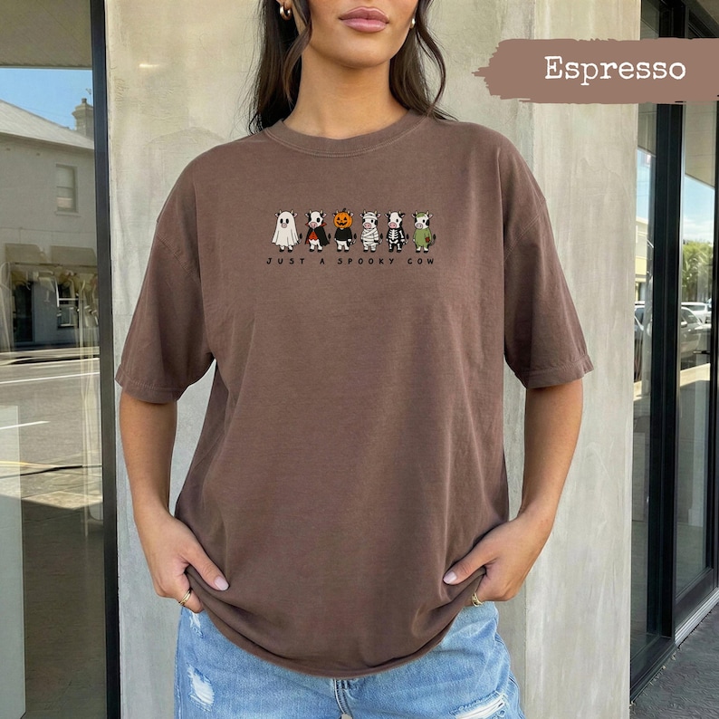 Brown t-shirt with cartoon cows in Halloween costumes and "Just A Spooky Cow" text.