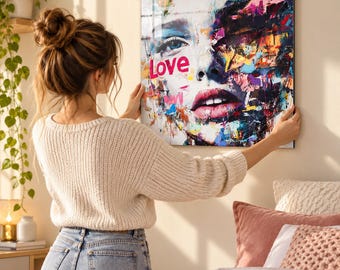 May include: A square wall art piece featuring a vibrant, abstract portrait of a face with one eye clearly defined and the other side composed of colorful paint splatters. The word Love is printed in bold pink letters on the left side.