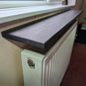 Peut inclure: Une étagère rectangulaire gris foncé avec un bord noir est montée au-dessus d'un radiateur blanc. L'étagère est placée sous une fenêtre, offrant un espace d'exposition ou de rangement. Une petite sculpture en bronze est sur le rebord de la fenêtre.