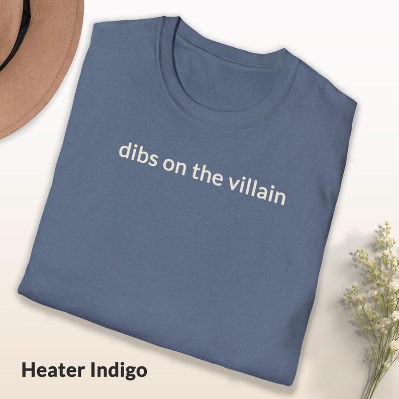 May include: A blue t-shirt with the text "dibs on the villain" in white. The shirt is folded and has a simple, casual design. The color is described as "Heater Indigo".
