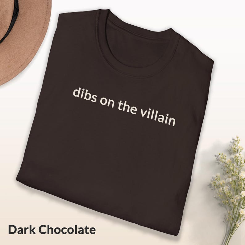 May include: Dark chocolate-colored t-shirt with the phrase "dibs on the villain" printed in white. The shirt is a crew neck style and is folded. The words "Dark Chocolate" are printed at the bottom of the image.