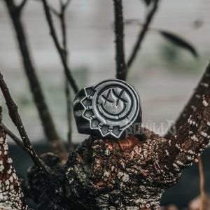 May include: A silver ring with a black smiley face design. The ring has a textured band with a raised design.