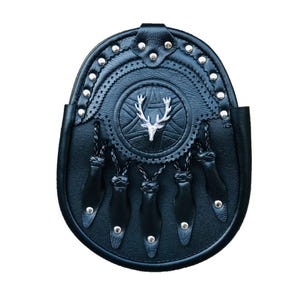 Puede incluir: Sporran de cuero negro con un emblema de cabeza de ciervo plateado y costuras decorativas. El sporran tiene flecos y est&aacute; adornado con tachuelas plateadas.