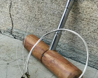 Puede incluir: Un enrollador de cuerdas de madera con una herramienta de enrollado de metal y un juego de cuerdas de guitarra plateadas.