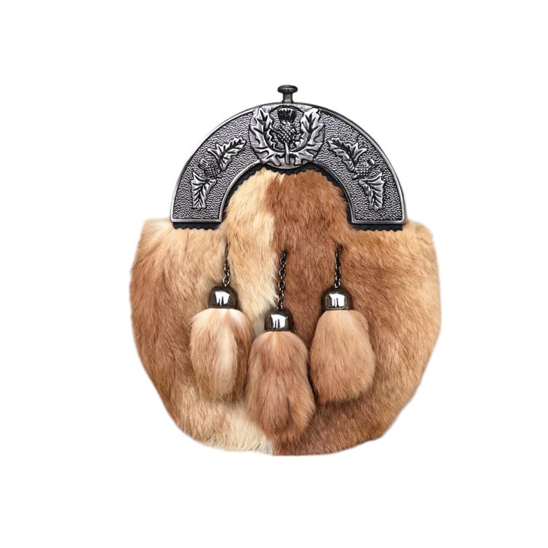 May include: A brown and tan fur sporran with a silver metal cantle. The cantle features a thistle emblem and decorative leaf patterns. Three matching fur tassels hang from the sporran.