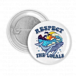 May include: A white button with a blue whale jumping over a wave with a sunset and palm trees in the background. The text "Respect the Locals" is written in blue letters below the whale.