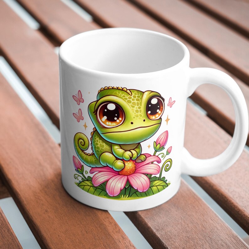 May include: White ceramic mug with a green cartoon chameleon with large eyes sitting on a pink flower. The chameleon is surrounded by pink flowers and butterflies.