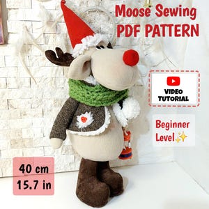 Peut inclure: Une peluche de renne de 40 cm de haut, portant un bonnet de Père Noël rouge, une écharpe verte et une veste marron. Le texte sur l'image indique "Moose Sewing PDF PATTERN", "VIDEO TUTORIAL" et "Beginner Level".