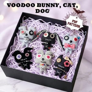 May include: A black gift box filled with shredded paper containing six handmade plush keychains shaped like bunnies, cats, and dogs. Each figure features button eyes, stitched mouths, and metal key rings. Text reads: VOODOO BUNNY, CAT, DOG and PDF PATTERN.