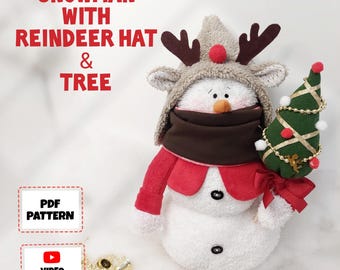 May include: A plush snowman wearing a reindeer hat and a red scarf, holding a small green Christmas tree. The snowman has a brown scarf and a carrot nose. The image includes the text "Snowman with Reindeer Hat & Tree".