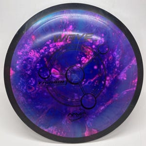 May include: A disc golf disc with a black rim and a vibrant, swirling design in shades of purple, pink, and blue. The disc features the word "WAVE" in pink, along with other text and a circular graphic. The brand logo "MVP" is visible.