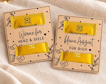 May include: Two rectangular kraft paper cards featuring black line drawings of tea bags and hearts. Each card holds two yellow Sonnentor tea packets. The left card reads "Wärme für HERZ & SEELE" and the right card reads "kleine Auszeit FÜR DICH".