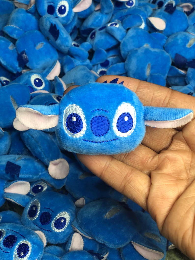 Op de afbeelding: Een close-up van een blauw pluche speelgoed met geborduurde ogen en een gestikte glimlach. Het speelgoed is gevormd als een cartoonfiguur met grote oren. Het speelgoed is omringd door andere vergelijkbare pluche speelgoed.