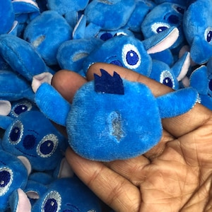 Op de afbeelding: Een stapel blauwe pluche vingerpoppen met geborduurde ogen en een gestikte mond. De poppen zijn gevormd als een cartoonfiguur met grote oren.