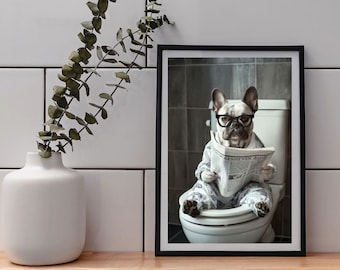 Puede incluir: Impresión enmarcada de un bulldog francés con gafas y pijama, sentado en un inodoro leyendo un periódico. La impresión está en un marco negro y colocada sobre una superficie de madera.