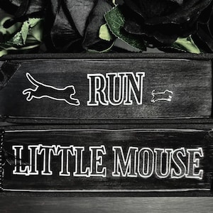 May include: Two stacked black books with white text and graphics on the spines. The top spine features a cat silhouette, the word RUN, and a small mouse silhouette. The bottom spine features the text LITTLE MOUSE in a bold, outlined font.