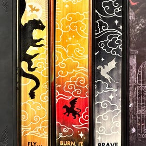 May include: Three fantasy novel book spines with a yellow, orange, and black background. The spines feature a dragon, a griffin, and a phoenix with the titles "Fly... or Die.", "Burn. It. Down.", and "Brave the Dark."