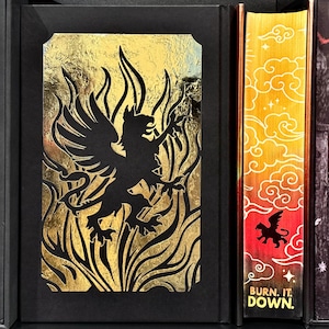 May include: A black and gold book cover with a black griffin silhouette in a gold flame design. The spine of the book has a gold and orange gradient with a black griffin silhouette and the text "BURN. IT. DOWN."