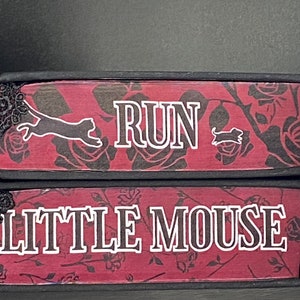 May include: Two stacked rectangular blocks with a dark red and black rose pattern. The top block features the white text RUN with a cat and mouse silhouette. The bottom block features the white text LITTLE MOUSE. Both have black lace trim.