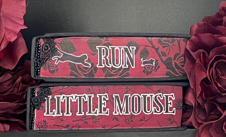 May include: Two stacked rectangular blocks with a dark red and black rose pattern. The top block features the white text RUN with a cat and mouse silhouette. The bottom block features the white text LITTLE MOUSE. Both have black lace trim.