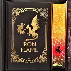 May include: A black book cover with gold accents featuring a dragon with flames and the title "IRON FLAME" with the words "BOOK II" below. The spine of the book is red and orange with a gold dragon and the words "BURN IT DOWN."