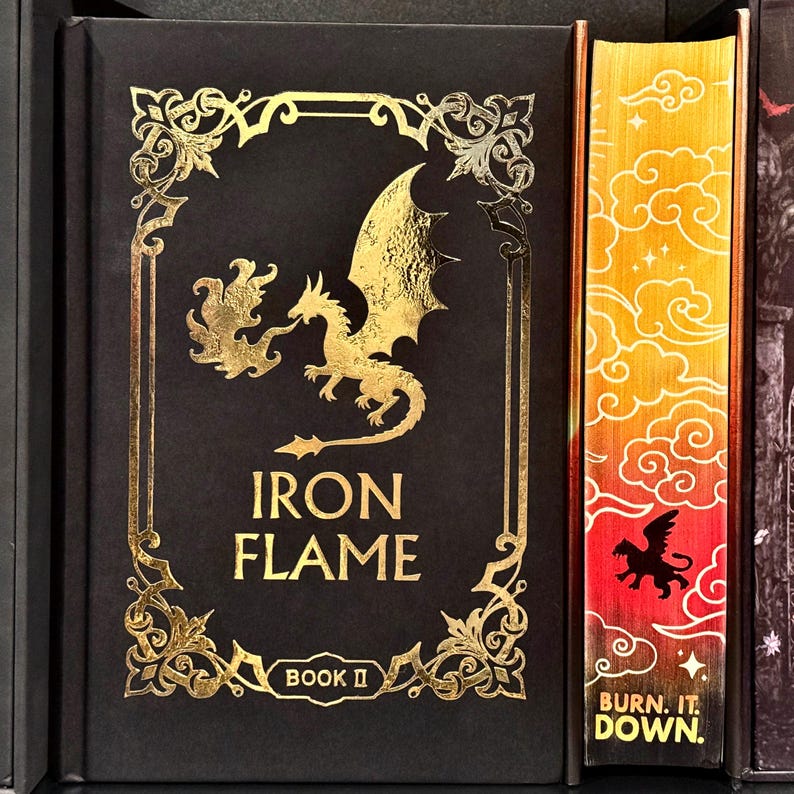 May include: A black book cover with gold accents featuring a dragon with flames and the title "IRON FLAME" with the words "BOOK II" below. The spine of the book is red and orange with a gold dragon and the words "BURN IT DOWN."