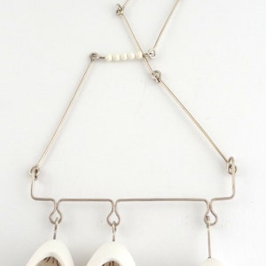 May include: A silver necklace with three white ceramic pendants, each containing small white pearls. The pendants are shaped like teardrops and have a delicate, intricate design.