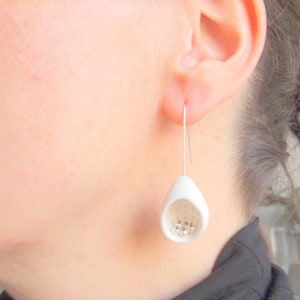 May include: White ceramic earrings with a teardrop shape and small white beads inside. The earrings are hanging from silver hooks.