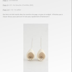 May include: A pair of white ceramic earrings with a small hole in the bottom and a silver wire hanging from the hole. The earrings are shaped like an egg and have a small cluster of silver beads inside. The earrings are hanging against a white background.